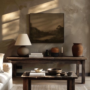 Puede incluir: Una mesa de madera r&uacute;stica con una l&aacute;mpara, libros y un jarr&oacute;n. La mesa est&aacute; frente a una pared con una pintura de un paisaje. La mesa est&aacute; decorada con un jarr&oacute;n, una vela y un libro.