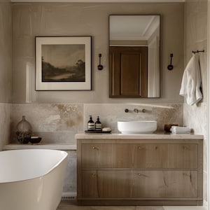 Puede incluir: Una ba&ntilde;era blanca se encuentra frente a un tocador de ba&ntilde;o con un lavabo de porcelana blanca y dos cajones. El tocador est&aacute; hecho de madera clara con herrajes de lat&oacute;n. Las paredes son de color beige claro y hay una impresi&oacute;n de paisaje enmarcada sobre el tocador.