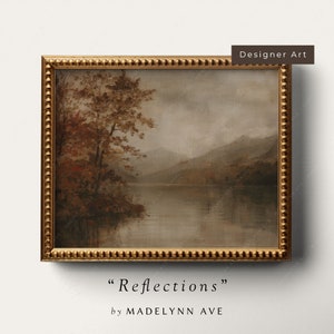 May include: A framed painting of a lake scene with a forest in the foreground and mountains in the background. The painting is in a gold frame with a beaded edge. The title of the painting is "Reflections" by Madelynn Ave.