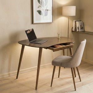 May include: A mid-century style desk with a laptop, a small drawer, and a matching chair. The desk has a dark brown finish and angled legs. The chair is upholstered in a light beige fabric. A framed botanical print hangs on the wall.