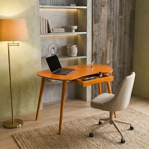 Op de afbeelding: Een niervormig houten bureau met een uitschuifbare lade, voorzien van een zwarte laptop, een klein inktpotje en een pen op het oppervlak. Het bureau heeft vier taps toelopende poten en een beige gestoffeerde bureaustoel op wieltjes.