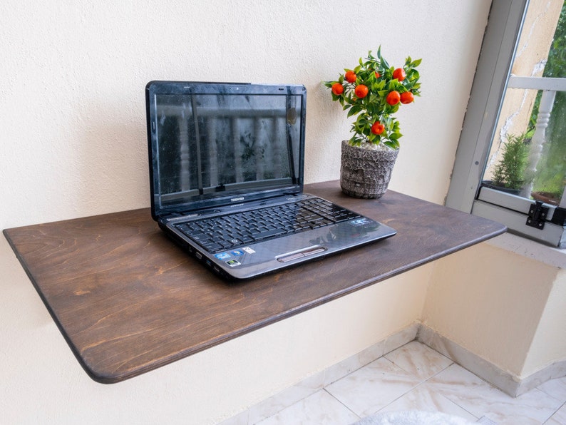 Here is Wall Mounted Foldable Home Office Desk Table! This Fold Down Small Space Saving Laptop Desk in the home office, balcony or kitchen perfectly complements the cozy atmosphere, offering a personalized touch to the workspace.