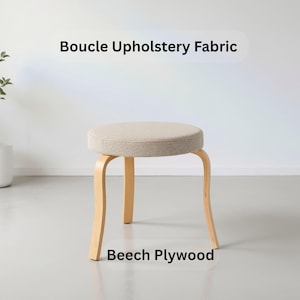 May include: A round stool featuring a beige bouclé upholstery fabric seat and three curved light-coloured beech plywood legs. The text Boucle Upholstery Fabric and Beech Plywood is visible in the image, identifying the materials used for the seat and base.