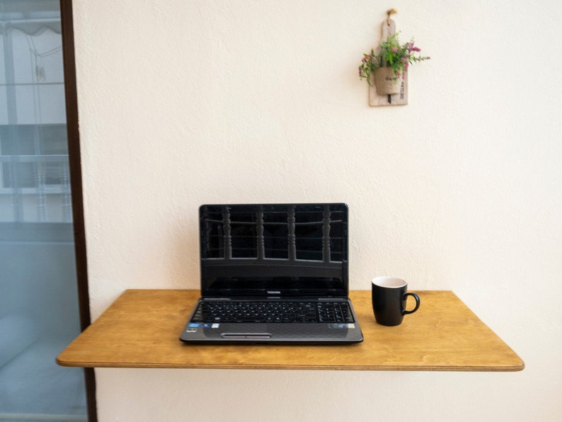 Here is Wall Mounted Foldable Home Office Desk Table! This Fold Down Small Space Saving Laptop Desk in the home office, balcony or kitchen perfectly complements the cozy atmosphere, offering a personalized touch to the workspace.