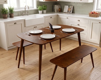 May include: A dark wood dining table with rounded corners and two matching benches. The table is set with four white plates and silver cutlery. The furniture features tapered legs and a smooth finish, positioned on a light wood floor.