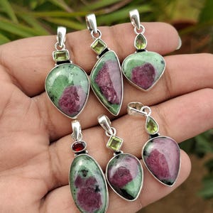 Puede incluir: Colección de colgantes de piedras preciosas con engarces de plata. Los colgantes presentan combinaciones de rubí y piedra verde en varias formas, incluyendo ovaladas, de lágrima y de corazón. Algunos colgantes tienen pequeñas piedras verdes o rojas.