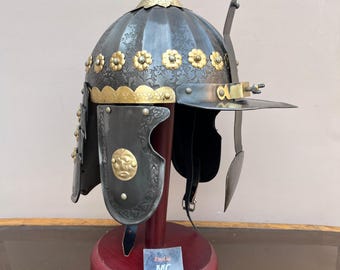 May include: A black and gold helmet with intricate floral designs and a brass chin strap. The helmet is on a wooden stand with a label that reads "Etsy.com MC Martin Craft".