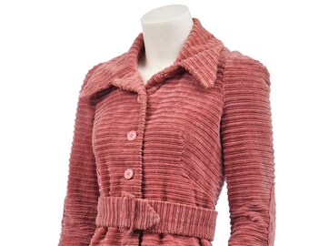 May include: A long-sleeved, pink corduroy jacket with a belt and button closure. The jacket has a pointed collar and pockets.