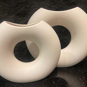 May include: Two white ceramic vases with a donut shape. The vases are textured and have a hole in the center.
