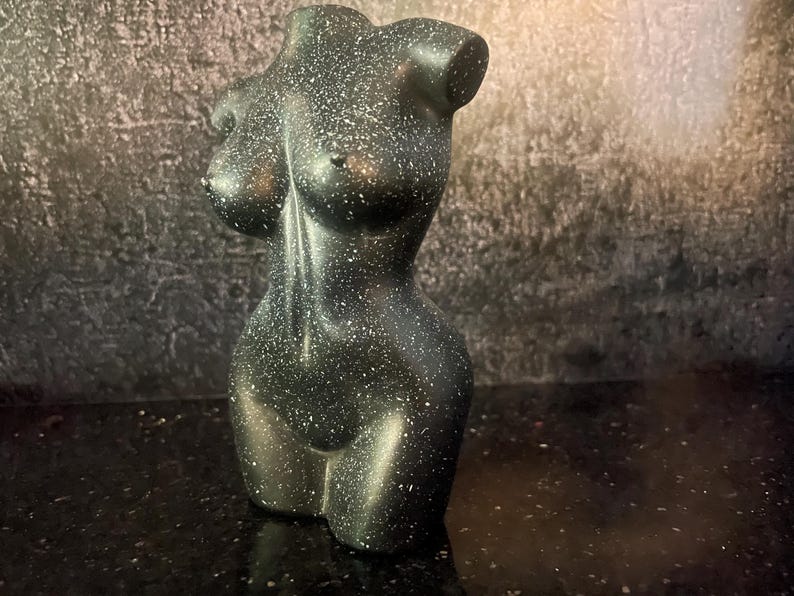 Może przedstawiać: Czarna i zielona, nakrapiana ceramiczna rzeźba torsu.