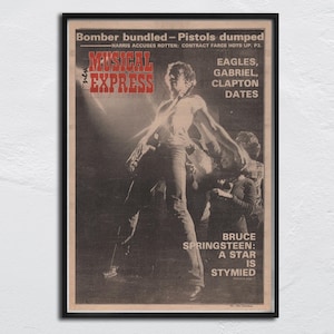 Puede incluir: Una portada de revista vintage enmarcada con una imagen en blanco y negro de un músico. La revista se titula "MUSICAL EXPRESS" en rojo y blanco. El texto incluye "Bomber bundled - Pistols dumped" y "Bruce Springsteen: A star is stymied".