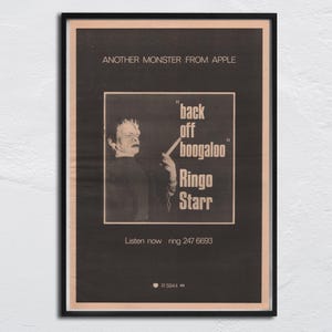 Puede incluir: Póster vintage enmarcado con fondo negro. En la parte superior, el texto "ANOTHER MONSTER FROM APPLE". El póster presenta una imagen en blanco y negro de un hombre con el texto "back off boogaloo Ringo Starr". En la parte inferior, "Listen now ring 247 6693".