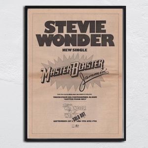 Könnte beinhalten: Ein gerahmtes Vintage-Poster mit Stevie Wonders Single "Master Blaster Jammin'". Das Poster hat einen beigefarbenen Hintergrund mit schwarzem Text, einschließlich des Songtitels und Albuminformationen. Das Poster ist in einem schwarzen Rahmen gerahmt.