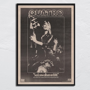 Puede incluir: Póster enmarcado en blanco y negro con la banda "Quatro". La imagen muestra a una mujer con una guitarra. El texto en el póster dice "The Wild One" y "Suzi's new album on RAK".