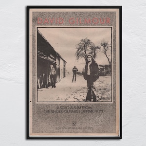 Puede incluir: Póster vintage enmarcado con David Gilmour, cantante y guitarrista de Pink Floyd. La imagen en blanco y negro muestra a Gilmour en un entorno rural. El texto en la parte superior dice "DAVID GILMOUR" y debajo, "A SOLO ALBUM FROM THE SINGER GUITARIST OF PINK FLOYD."