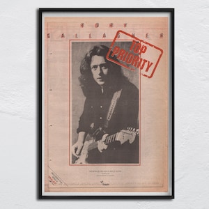 Può includere: Una foto in bianco e nero di Rory Gallagher, un musicista, che suona la chitarra. La foto è su una pagina di rivista vintage con il testo "Rory Gallagher" e "Top Priority" in rosso.