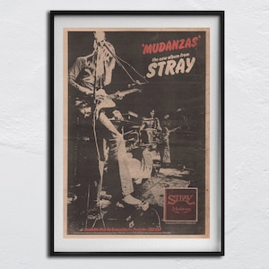 May include: Framed vintage poster advertising the album 'Mudanzas' by Stray. The poster has a monochrome image of the band performing, with red and white text for the band name and album title. The Stray Mercury logo is also displayed.