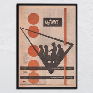 Peut inclure: Affiche vintage encadrée avec le groupe Buzzcocks. Le design comprend des cercles orange, un triangle noir et le texte "a different kind of tension". Le nom du groupe est en blanc sur un rectangle noir.