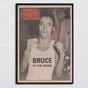 May include: Black framed poster featuring a vintage magazine cover. The magazine is titled "MUSICAL EXPRESS" with a black and white image of a man wearing a tank top that says "BRUCE IS THE WORD". Additional text is visible.