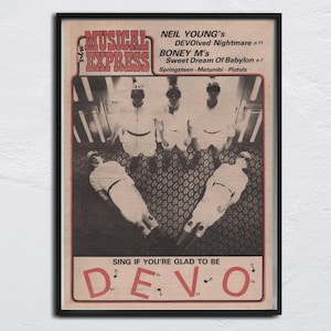 Peut inclure: Une couverture de magazine vintage encadrée, avec un cadre noir, représentant le groupe Devo. La couverture sépia comprend le texte "Musical Express" et des titres de chansons. L'image montre des membres du groupe en tenues blanches.