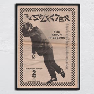 May include: Black and white poster featuring "The Selecter" band. The poster includes the text "Too Much Pressure" and "Album Out Now On 2 Tone". A man in a suit is leaning over. The poster has a checkered border.