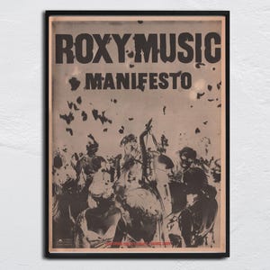 May include: Framed vintage poster for Roxy Music's album "Manifesto." The poster features the band's name and album title in bold, black letters. A sepia-toned image of a crowd is below the text. The poster is in a black frame.