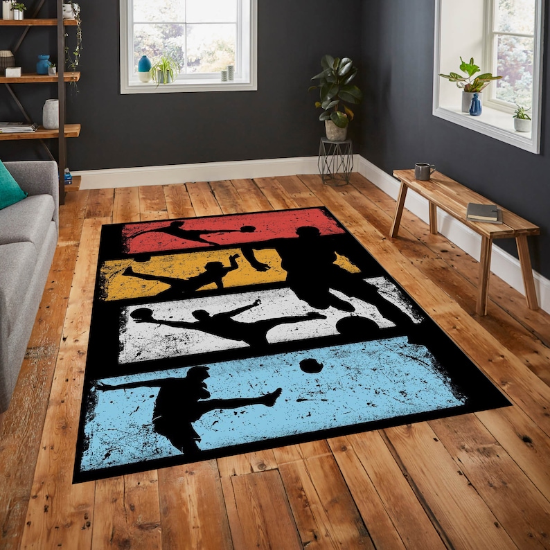 May include: A black and white rug with a retro design featuring silhouettes of soccer players kicking a ball. The rug has a distressed look with a faded background in shades of red, yellow, white, and blue.