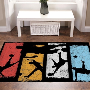 May include: A black and white rug with a distressed look featuring five silhouettes of people playing soccer. The rug is divided into five vertical sections, each with a different color background: red, yellow, white, blue, and blue.