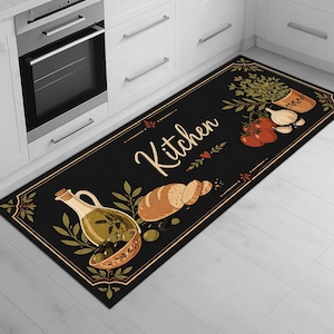 Puede incluir: Alfombra de cocina rectangular negra con un borde decorativo. La alfombra presenta ilustraciones de aceite de oliva, aceitunas, pan, tomates, ajo y hierbas. La palabra "Kitchen" está escrita en cursiva en el centro de la alfombra.
