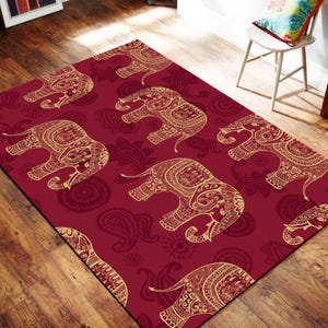 May include: A rectangular area rug featuring a deep red background with a repeating pattern of gold-colored elephants. Each elephant is decorated with intricate, swirling line work and floral-inspired motifs, creating a dense, ornate design.