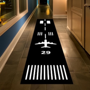 May include: A long, rectangular black runner rug featuring a white graphic design that mimics an airport runway. The design includes a central airplane silhouette, the number 29, dashed centerline markings, and white threshold stripes.