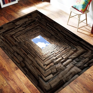 May include: A rectangular area rug featuring a 3D optical illusion print of a deep, dark brown stone well or tunnel. The design creates a perspective effect leading toward a bright, square opening at the center that reveals a clear blue sky.