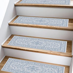 K&ouml;nnte beinhalten: Mehrere hellblaue und wei&szlig;e Treppenl&auml;ufer mit floralem Muster. Die rechteckigen L&auml;ufer liegen auf Holztreppen. Das Design zeigt ein zentrales Medaillon und Bord&uuml;rendetails, die der Treppe eine dekorative Note verleihen.