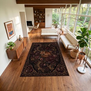 Puede incluir: Una alfombra rectangular con fondo oscuro que presenta una ilustraci&oacute;n central de un zorro durmiendo rodeado de intrincados patrones florales y bot&aacute;nicos en tonos rojo intenso, dorado y marr&oacute;n, colocada sobre un suelo de madera en una sala.
