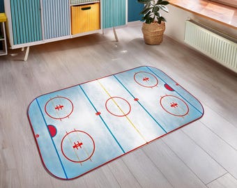 May include: A rectangular area rug featuring a light blue ice hockey rink design with red face-off circles, a yellow centre line, and blue zone lines. The rug has rounded corners and a red border, mimicking the layout of a professional rink.