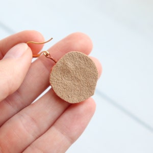 May include: A pair of brown leather earrings with a gold hook. The earrings are round and have a textured surface.