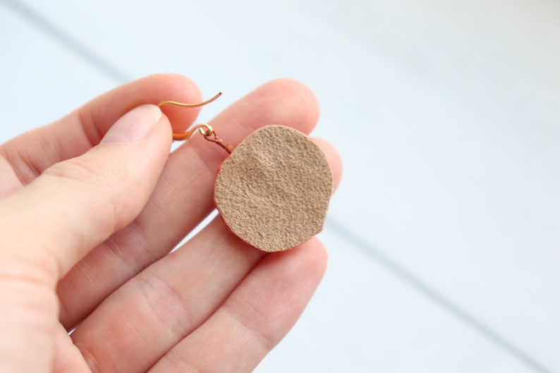 May include: A pair of brown leather earrings with a gold hook. The earrings are round and have a textured surface.