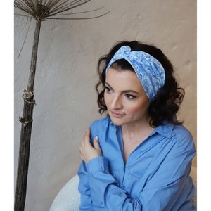 May include: A woman wearing a blue and white patterned headband. The headband is knotted on top of her head. She is wearing a blue shirt.