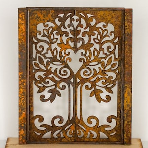 Könnte beinhalten: Eine rostige Metallwanddekoration mit einem ausgeschnittenen Design eines Baumes mit filigranen Ästen und Blättern. Der Baum ist mittig im Bild platziert und hat eine Herzform in der Mitte des Stammes.