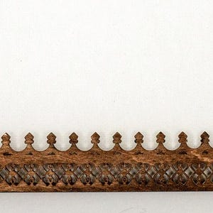 May include: A wooden decorative trim with a repeating pattern of pointed arches and a carved design. The trim is brown and has a distressed finish.