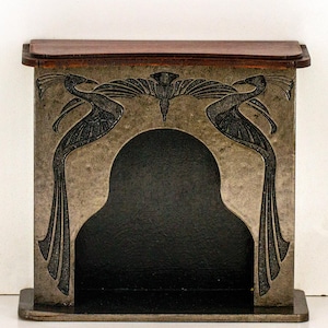 Puede incluir: Una chimenea decorativa con un acabado negro y gris. La chimenea presenta un diseño tallado de dos pájaros con las alas extendidas y un motivo floral.