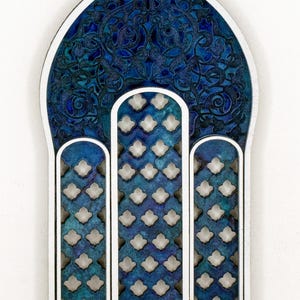 May include: A blue and white wooden wall hanging with a decorative, intricate design. The design features a traditional archway with a repeating pattern of small, diamond-shaped cutouts.