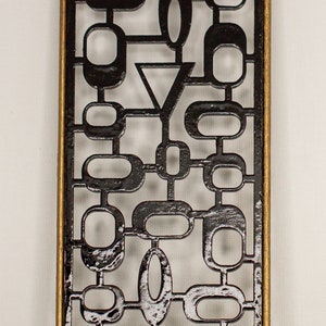 Könnte beinhalten: Eine schwarze Wanddekoration aus Metall mit einem geometrischen Muster aus Kreisen und Ovalen. Die Dekoration ist mit einem goldenen Metallrahmen versehen.