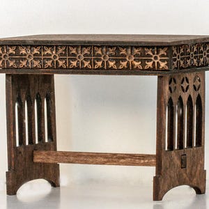 May include: A small, dark brown wooden table with a carved top and intricate, gothic-style legs. The table has a rectangular top with a carved design of repeating floral patterns.