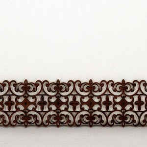 May include: A brown decorative border with a repeating pattern of swirls and geometric shapes. The border is made of a thin, delicate material and has a slightly distressed look.