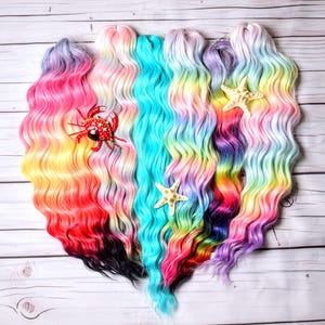 May include: Six strands of wavy hair extensions in various colors, including pink, blue, purple, and yellow. The hair is arranged in a heart shape and decorated with a red crab and two white starfish.