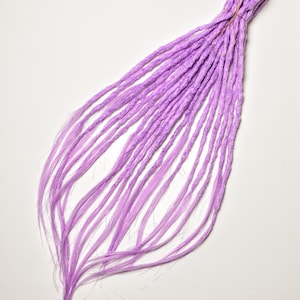 May include: A bundle of lavender-colored synthetic dreadlocks, tied together with a brown band. The dreadlocks are long and have a textured appearance, with a slight gradient in color from the roots to the tips.