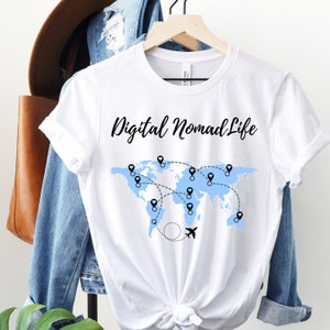 May include: White t-shirt with a blue world map and the text "Digital Nomad Life" in black. The map has pins and dotted lines connecting them, representing travel destinations. A small airplane icon is flying above the map.