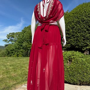 May include: A long, red, sheer skirt with gold and white embroidery. The skirt is tied at the waist with a white sash.
