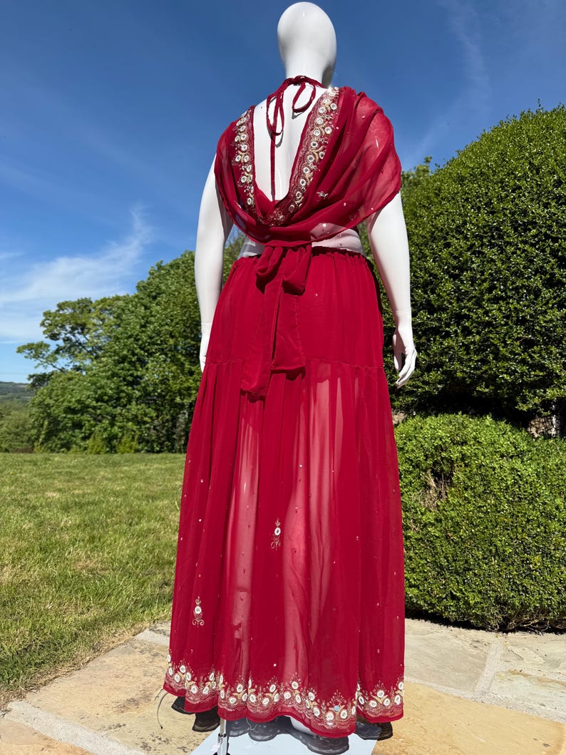 May include: A long, red, sheer skirt with gold and white embroidery. The skirt is tied at the waist with a white sash.